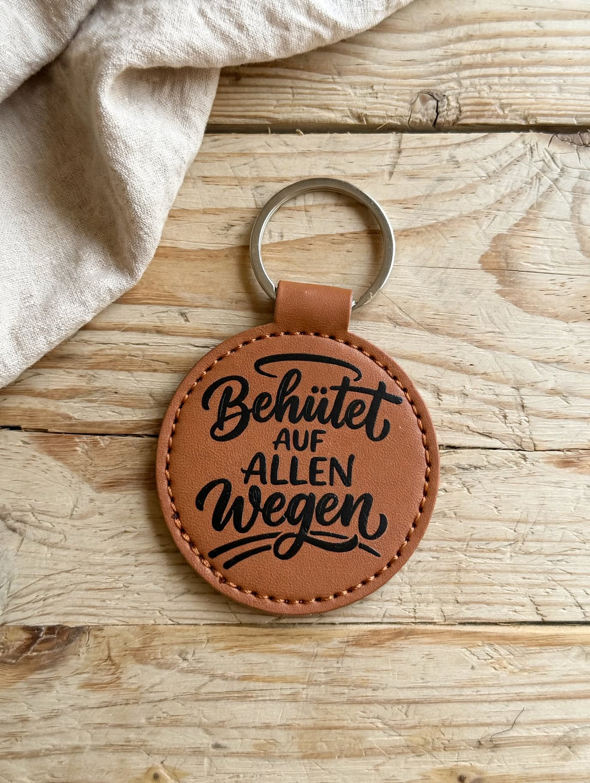 Schlüsselanhänger Behütet auf allen Wegen cognac - runder Kunstleder Anhänger mit schwarzem Spruch auf Holztisch - Geschenk Schutzengel Glücksbringer