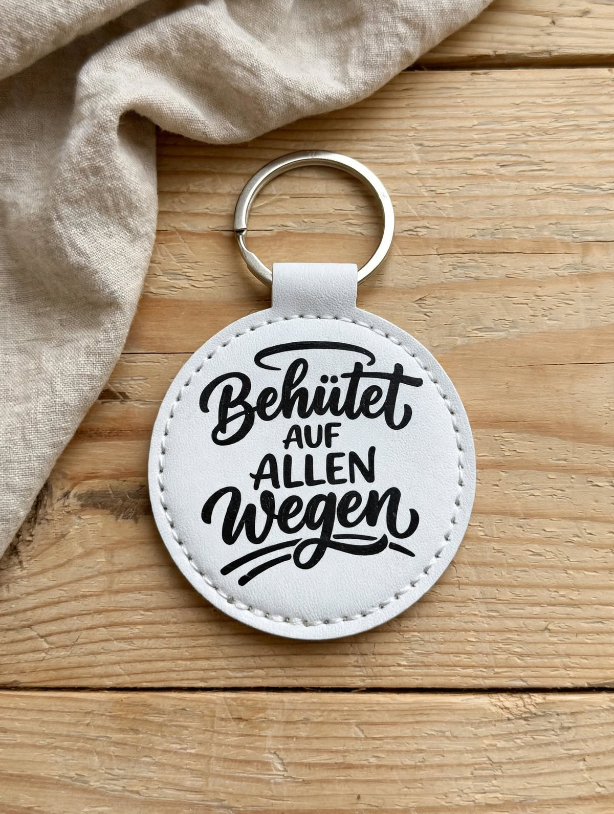Schlüsselanhänger Behütet auf allen Wegen weiss - runder Kunstleder Anhänger mit schwarzem Spruch - auf Holztisch - Geschenk Schutzengel Glücksbringer