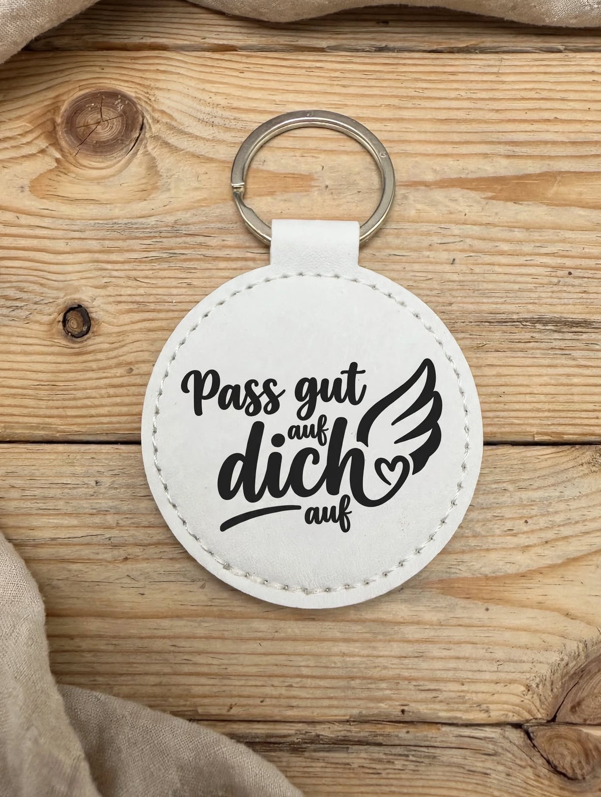 Schlüsselanhänger Pass gut auf dich auf schwarz - runder Kunstleder Anhänger mit weissem Aufdruck Engelsflügel und Herz - auf Holztisch mit Schlüssel und Portemonnaie - Geschenk Idee