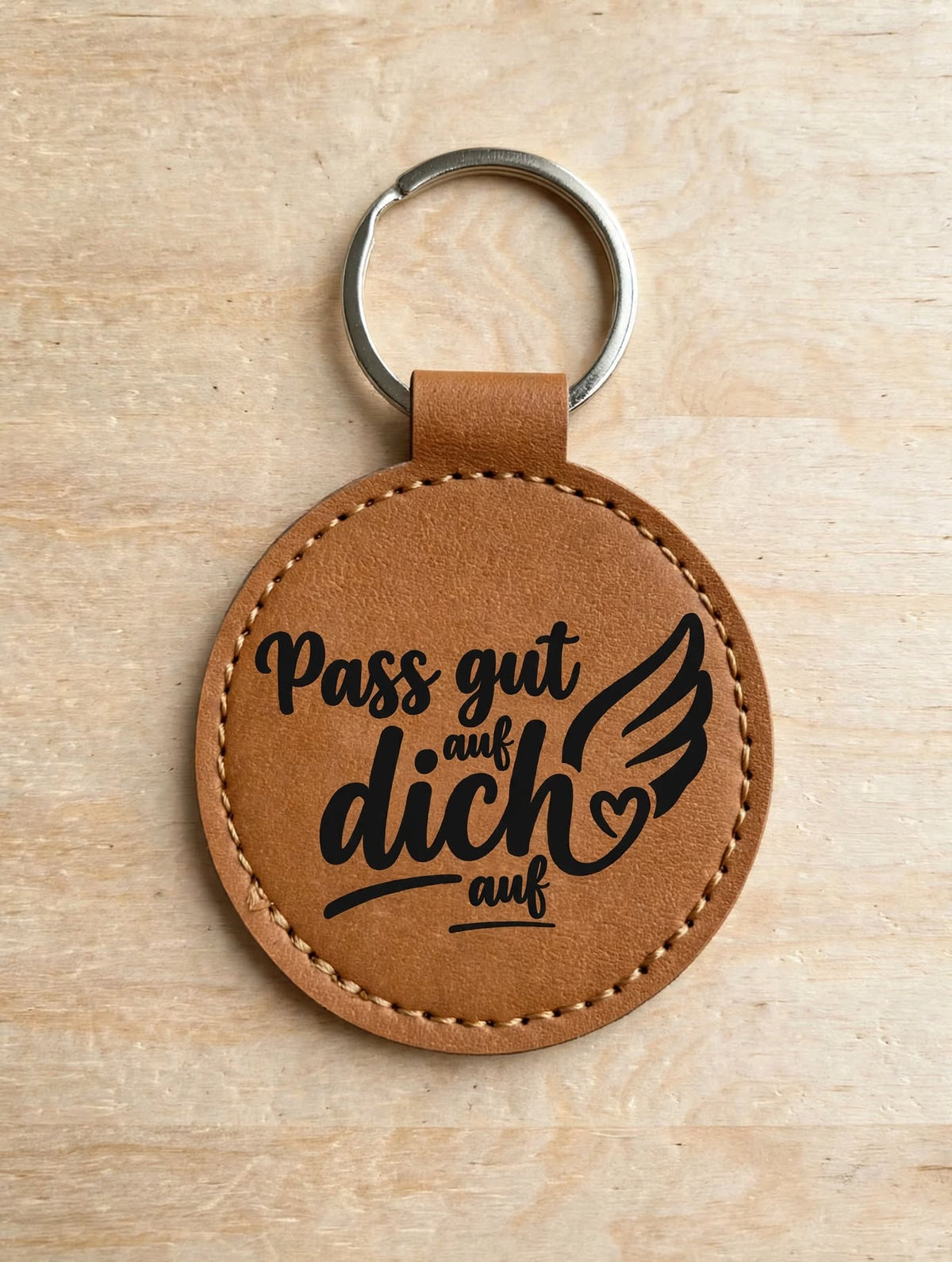 Schlüsselanhänger Pass gut auf dich auf dunkelbrauner- runder Kunstleder Anhänger mit schwarzem Aufdruck Flügel Herz - Nahaufnahme Detailansicht